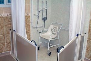 Salle de bain comprenant une douche PMR équipée de rampes, fauteuil et douchette parfaitement adaptée pour une personne à mobilité réduite